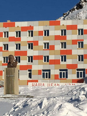 Een standbeeld van Lenin staat voor een kleurrijk gebouw in Barentsburg, omgeven door sneeuw.