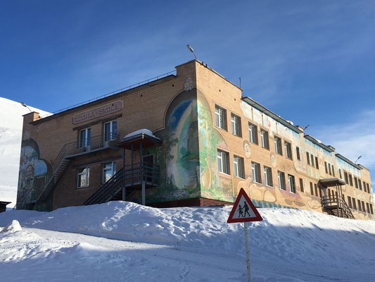 Een gebouw met muurschilderingen in Barentsburg, omringd door sneeuw en een blauwe lucht.