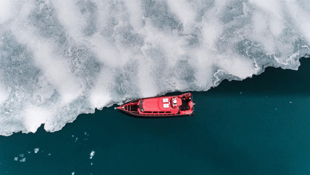 Een rode boot drijft langs een ijsschots in turquoise water.