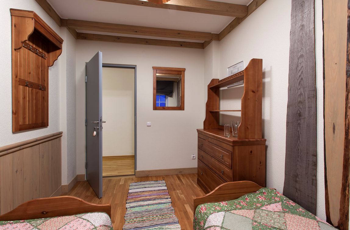 Een sfeervolle hotelkamer in Barentsburg met houten accenten, twee bedden met kleurrijke dekbedovertrekken en een eenvoudige kast. De kamer heeft een deur naar een andere ruimte en een vloerkleed, waardoor het een warme uitstraling heeft.