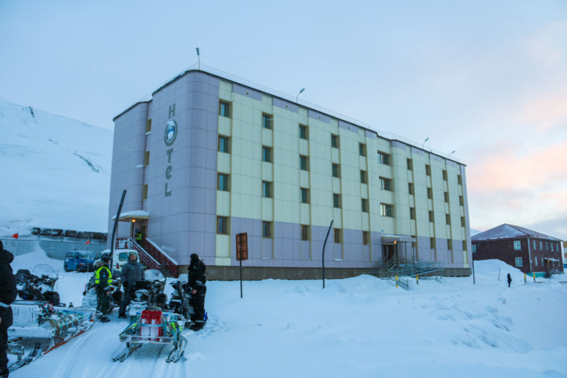 Het Hotel Barentsburg, een kleurrijk gebouw met de tekst 'HOTEL' aan de voorzijde, omgeven door sneeuw in een arctische omgeving.