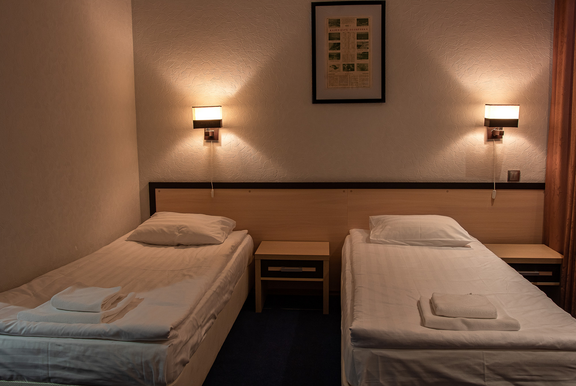 Interieur van een kamer in Hotel Barentsburg met twee eenpersoonsbedden, nachtkastje en verlichting