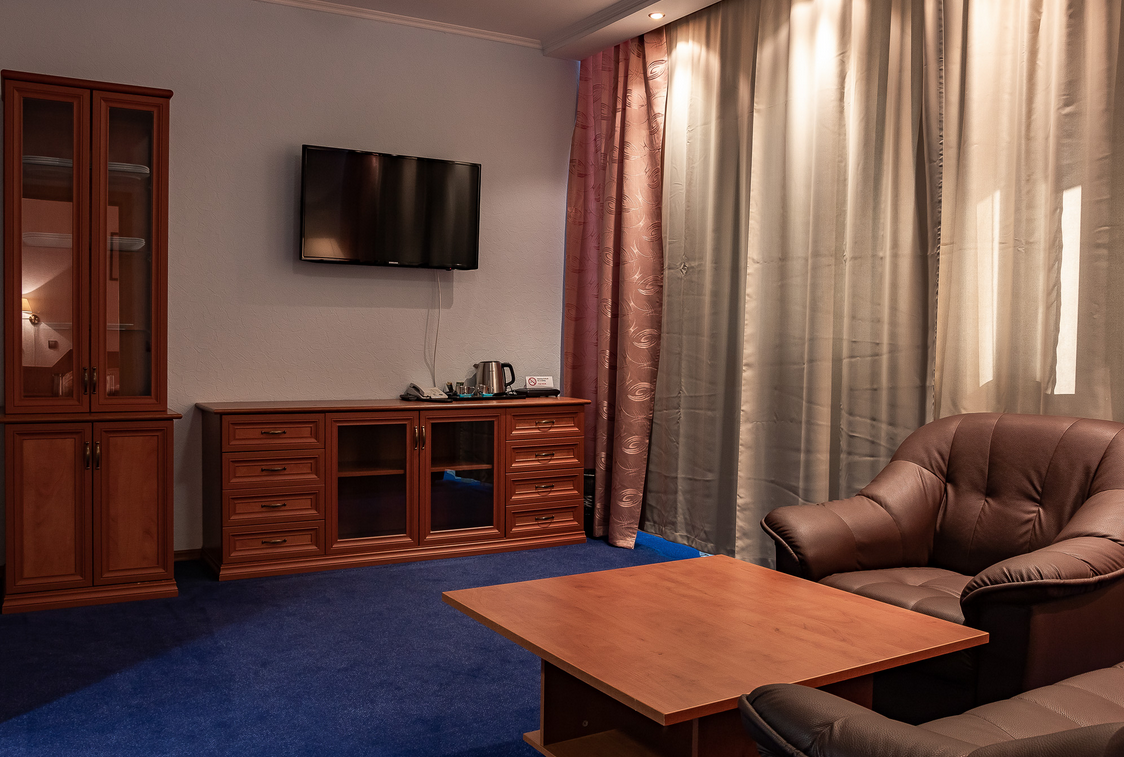 Interieur van een hotelkamer in Barentsburg met een televisie, een houten meubelstuk, een zitgedeelte met leren stoelen en gordijnen.