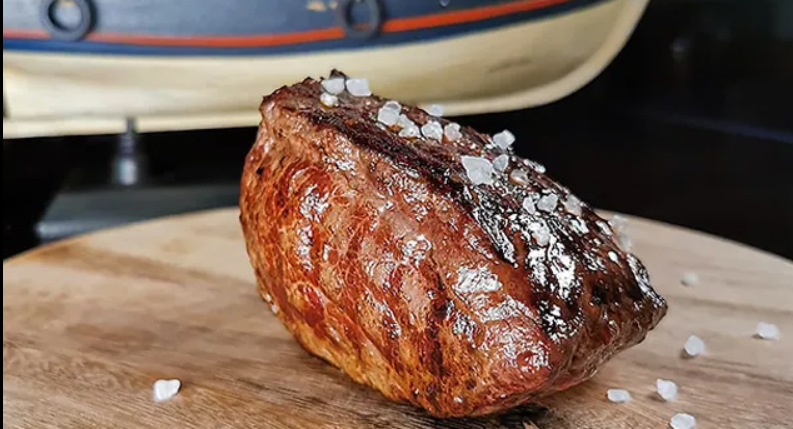 Gegrilde steak met een zilveren glans van zeezout, geserveerd op een houten snijplank, met een maritieme achtergrond.