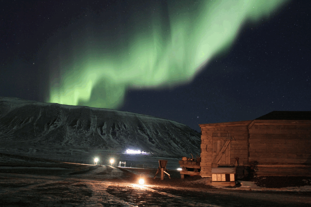 Een adembenemend uitzicht op het noorderlicht boven een besneeuwd landschap en een houten gebouw op Spitsbergen.