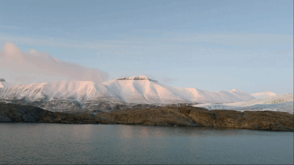Zicht op besneeuwde bergen met een blauwe lucht en kalme wateren in een fjord op Spitsbergen.