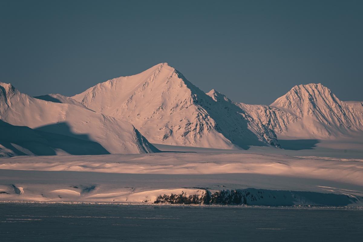 Bergen bedekt met sneeuw in het arctische landschap van Svalbard, met een zachte gloed van de zon die de toppen verlicht